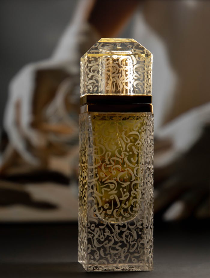 Vertical shot of an elegant perfume bottle with intricate gold patterns and a blurry background.