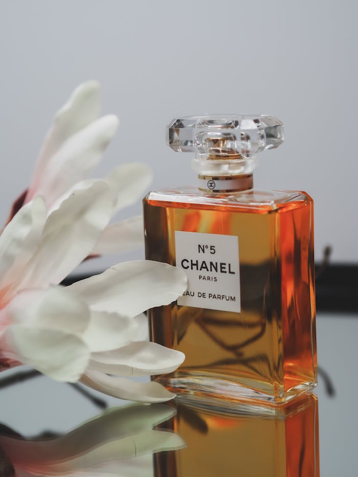 Chanel No. 5 perfume bottle on reflective surface with white petals in soft focus.