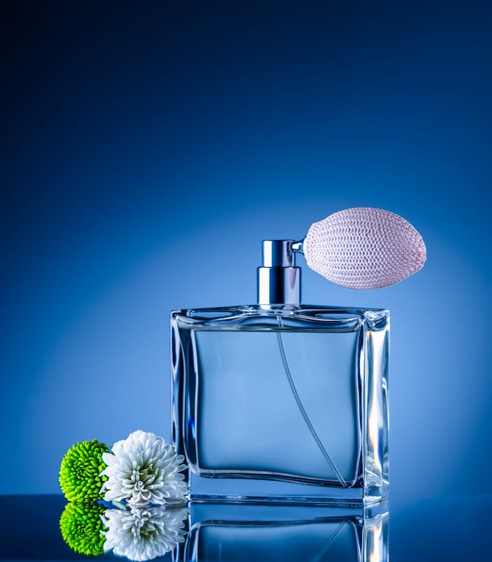 Sophisticated perfume bottle with atomizer surrounded by vibrant flowers on a reflective surface.